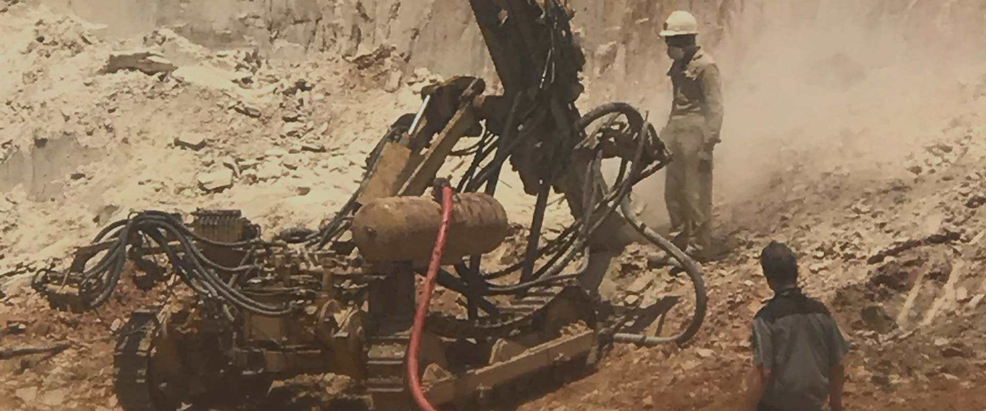 Drilling rig working a bench at the quarry face, dust rising